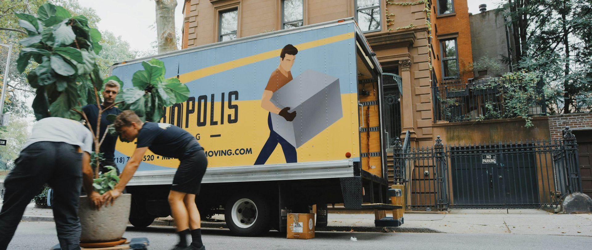 Movers unloading plants outside residential moving truck.